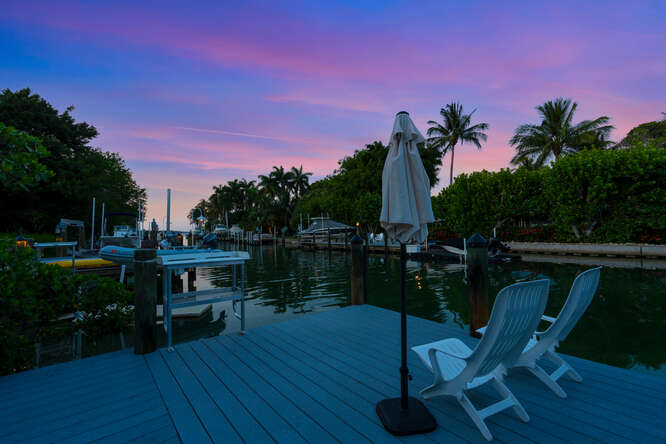 A dock with chairs and palm trees at sunset.